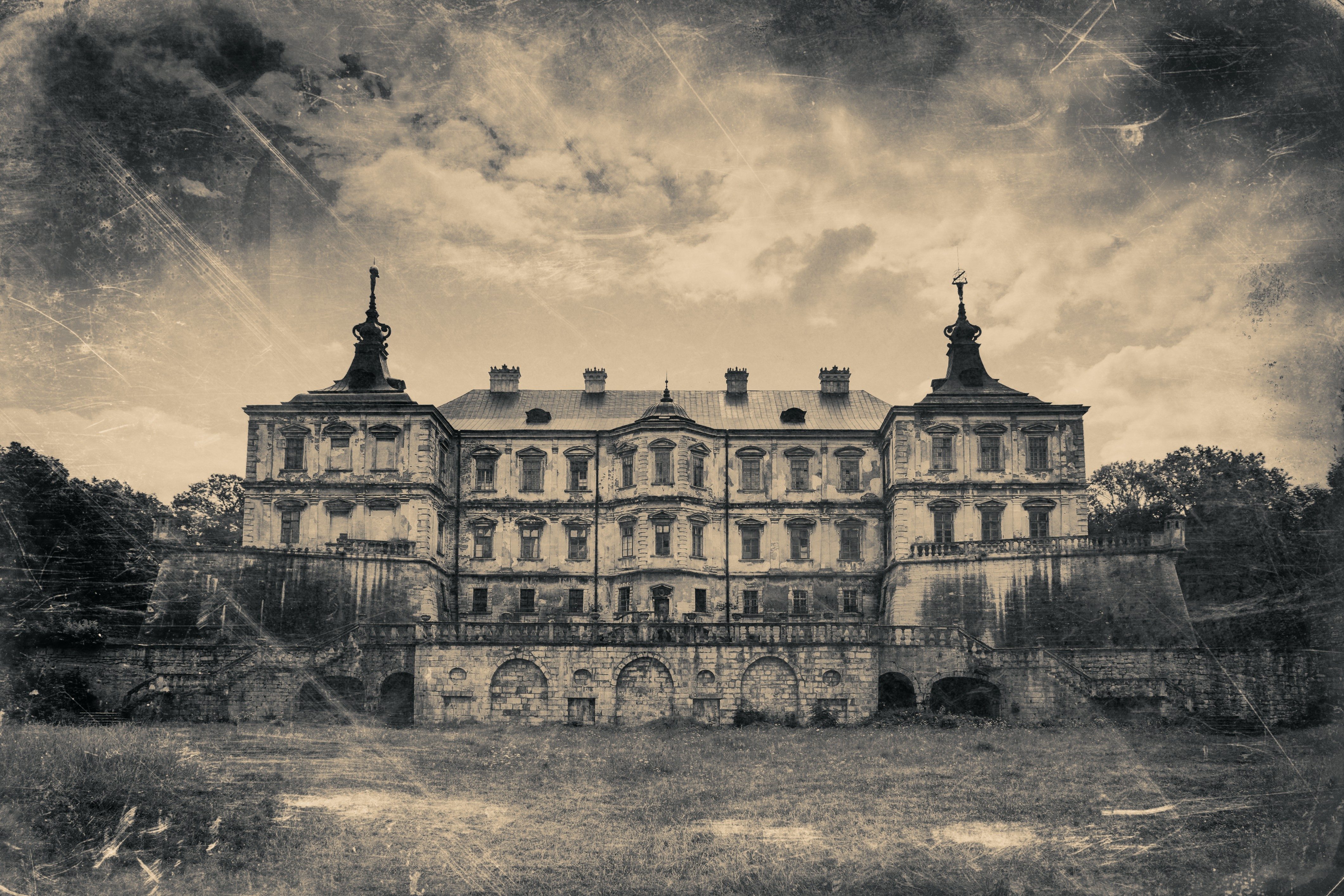 An aged castle stands silently, surrounded by trees under a cloudy sky, with visible wear and architectural details.
