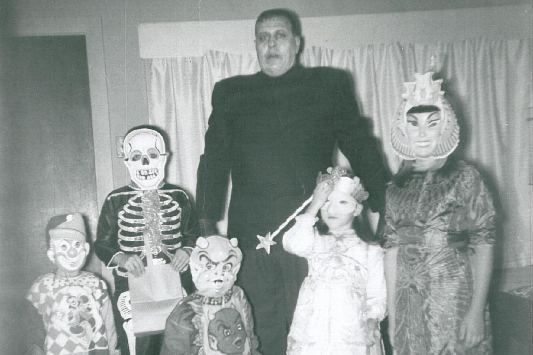 Group wears costumes, including masks and outfits, standing indoors against curtains.