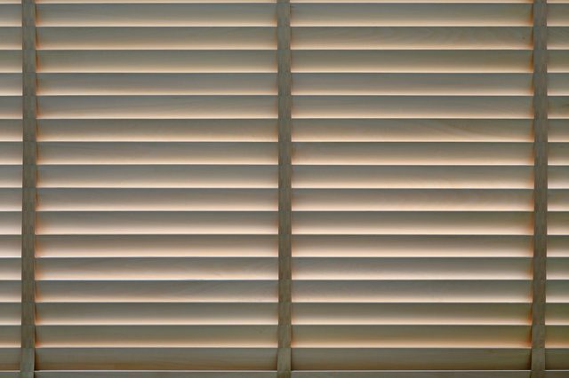 Horizontal wooden blinds partially open, allowing soft light to filter through; situated indoors.