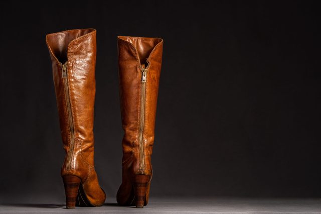 Brown leather knee-high boots stand upright against a dark background, zippers visible along the sides.