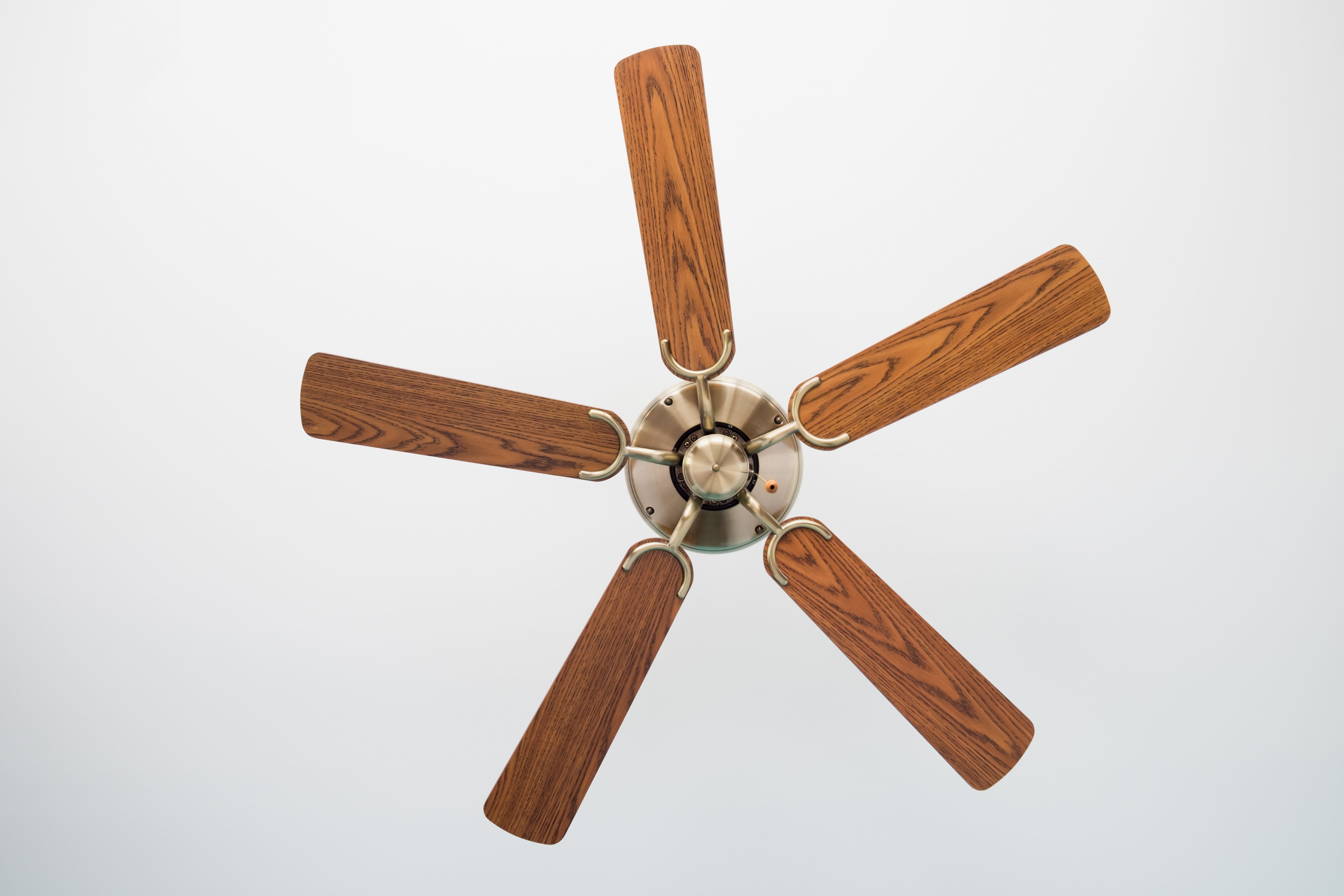 Ceiling fan with five wooden blades, stationary, against a white ceiling.