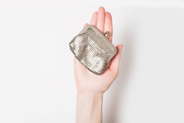 A hand holds a small, silver mesh coin purse against a plain, white background.