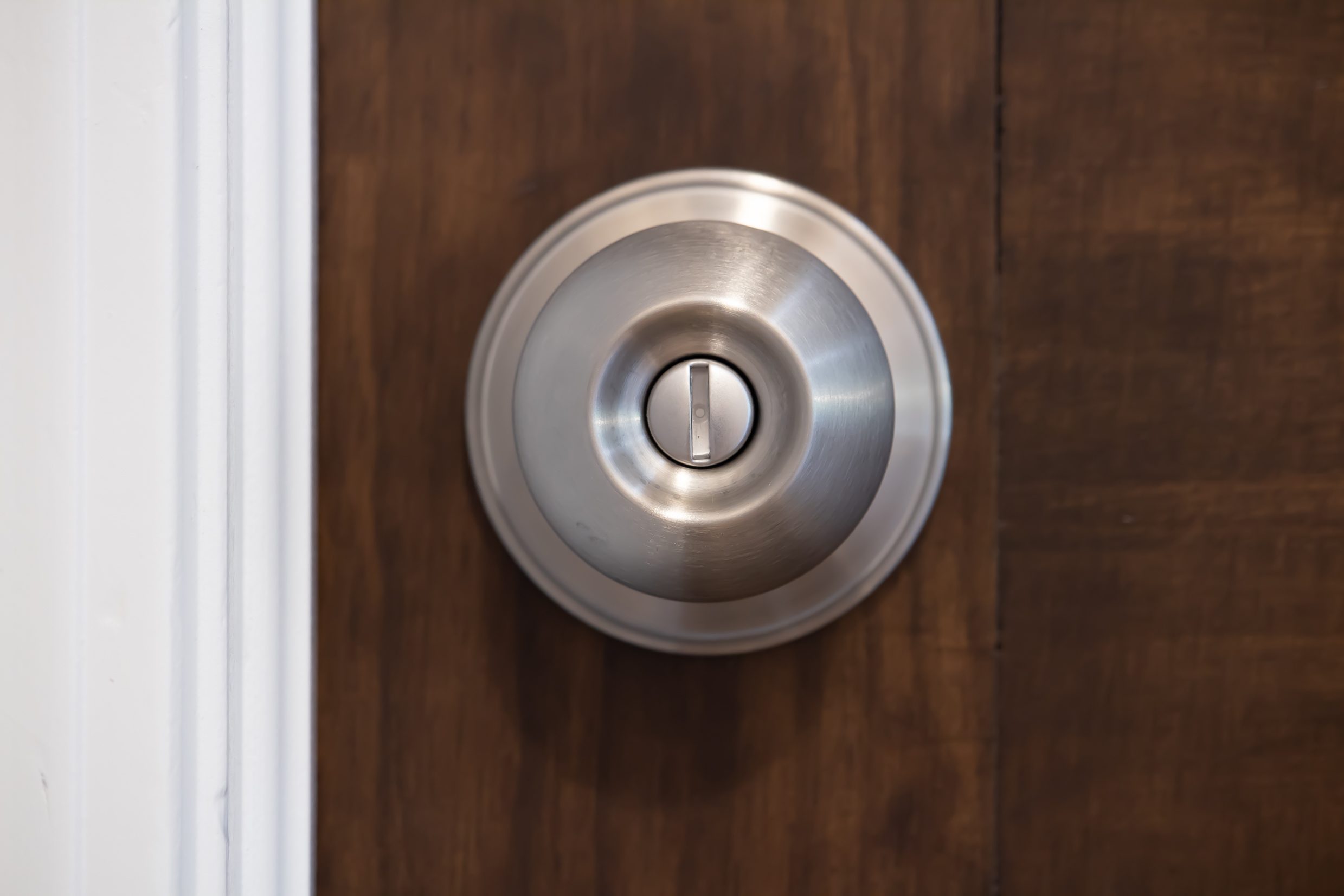 Silver doorknob with lock, situated on a wooden door, adjacent to a white door frame.