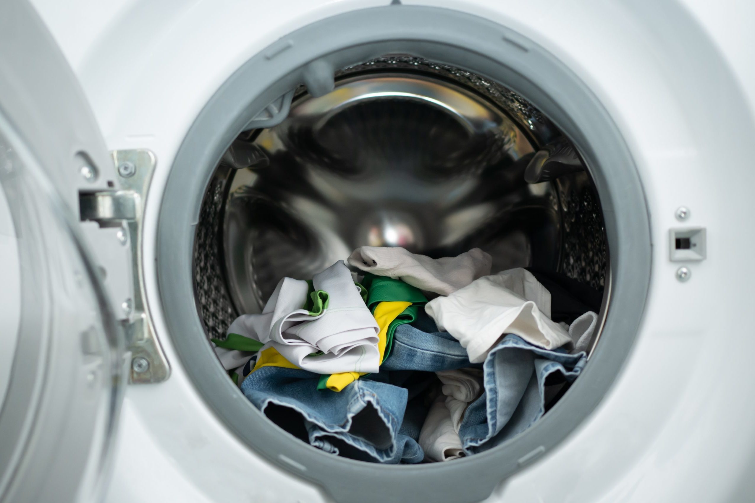 Clothes sit inside an open washing machine, ready for a cycle in a laundry room setting.