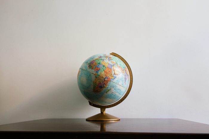 Globe model on dark wooden desk. White wall empty space background.