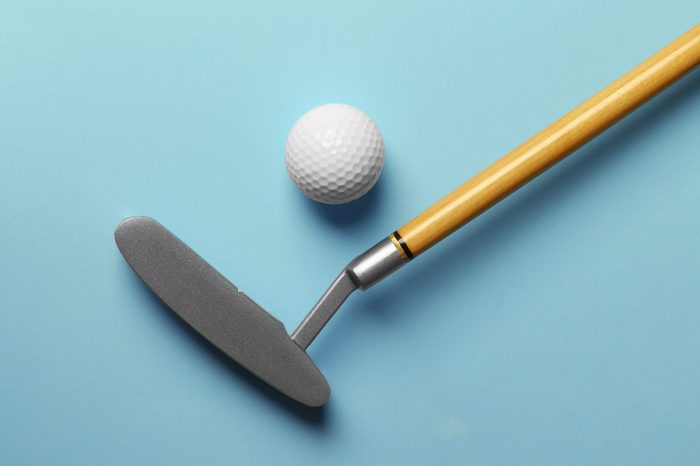 Golf ball and club on light blue background, flat lay. Space for text