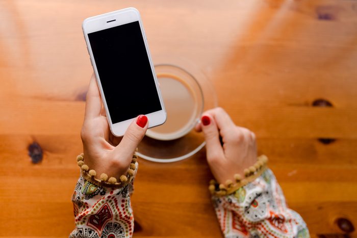 Closeup on hand using mobile smart phone, wooden desk background, mock up flat lay
