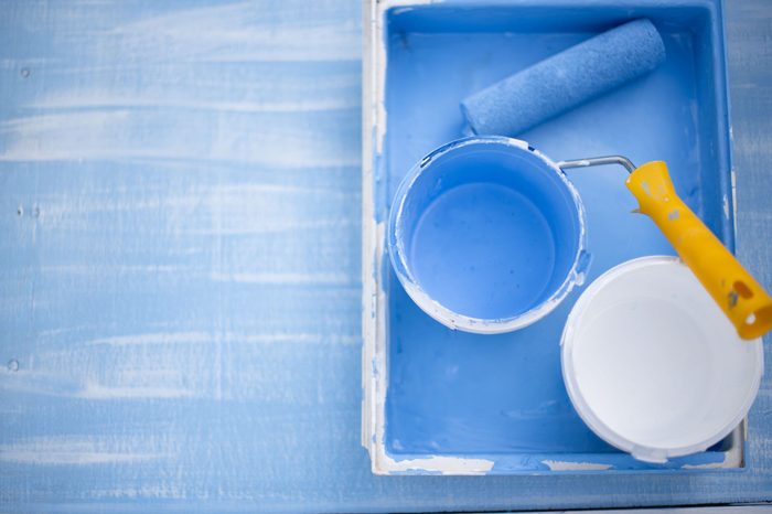 The roller for coloring lies in the tray with blue and white paint