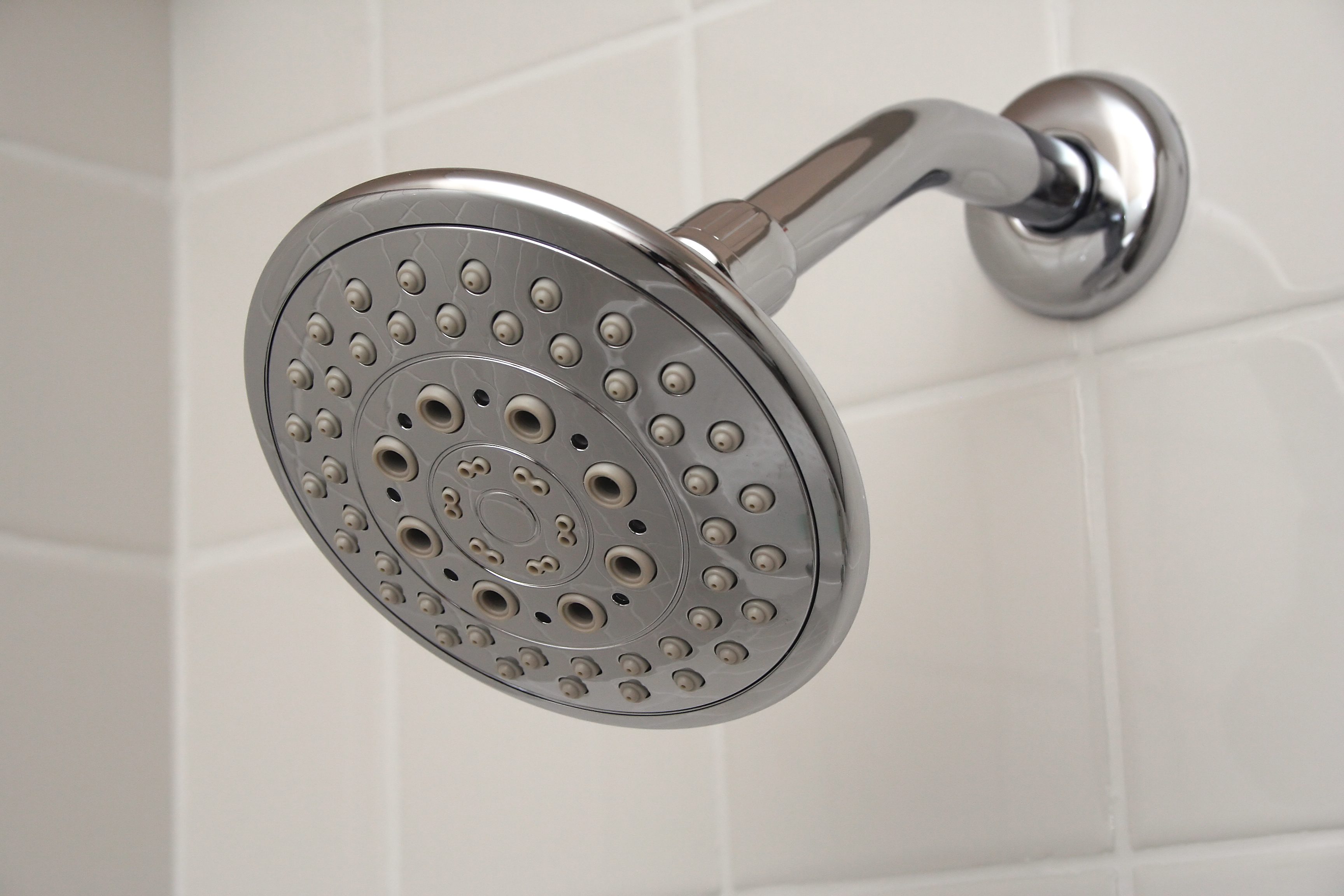 Showerhead mounted, angled downward, surrounded by white tiled wall.