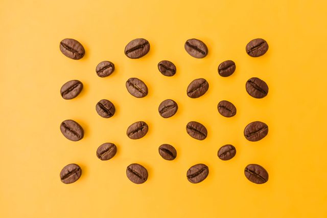 Coffee beans scattered evenly across a vibrant yellow background, creating a simple and striking contrast.