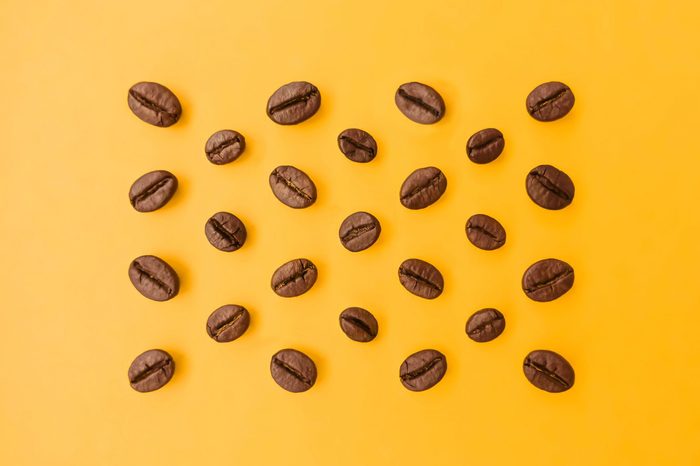 Select the best ideal coffee beans lay out on a bright orange background that emphasizes the beauty of coffee beans and perfectly blends in colors.