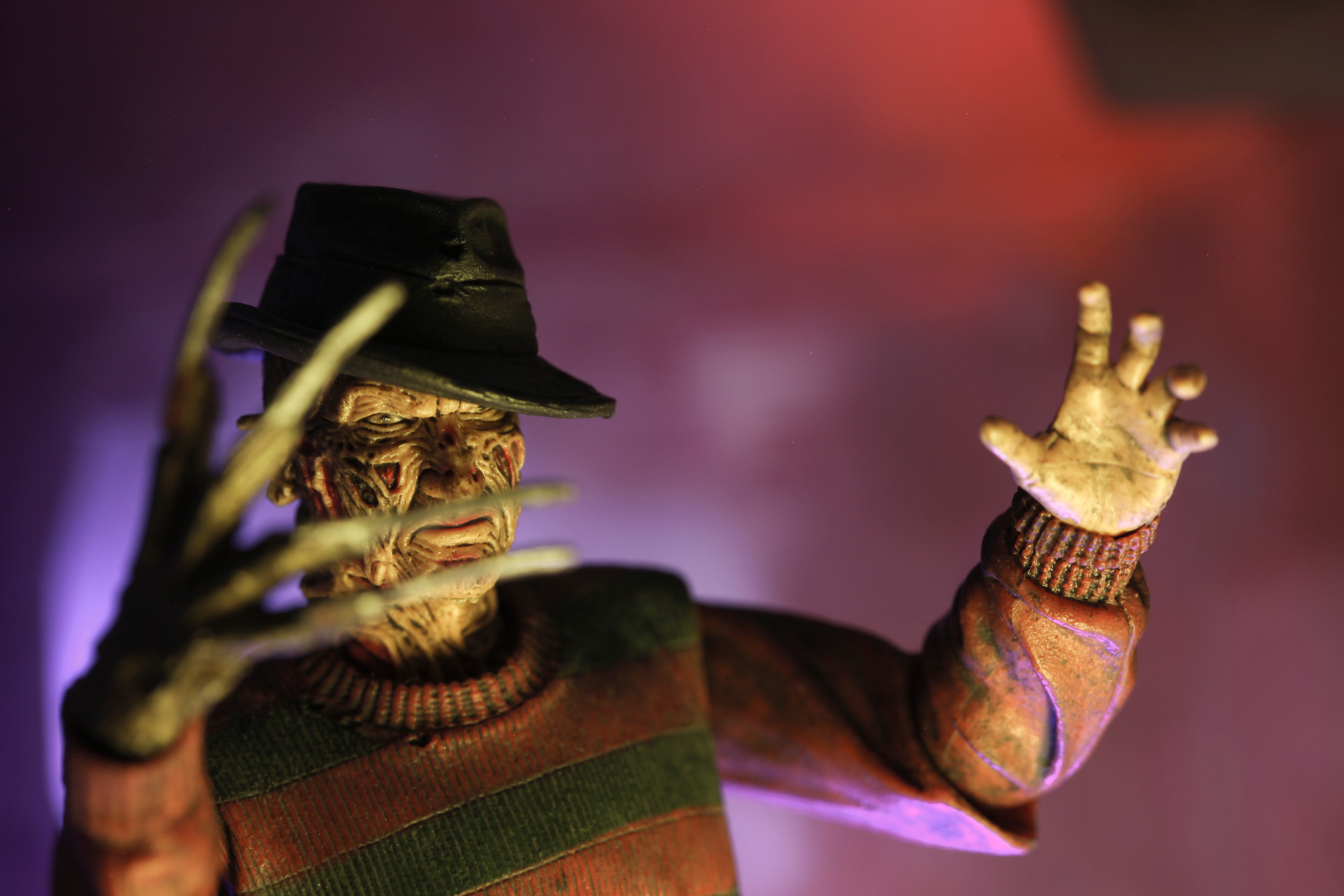 A horror figure with extended clawed fingers raises hands menacingly in a dim, colored light setting.