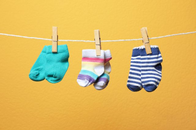 Three pairs of baby socks hang on a clothesline, clipped with wooden clothespins, against a bright yellow background.
