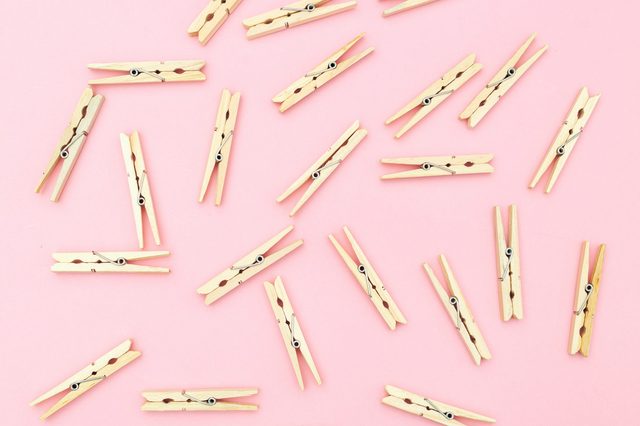 Wooden clothespins scattered randomly on a pink background.