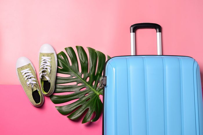 Suitcase, shoes and tropical leaf on color background. Travel concept