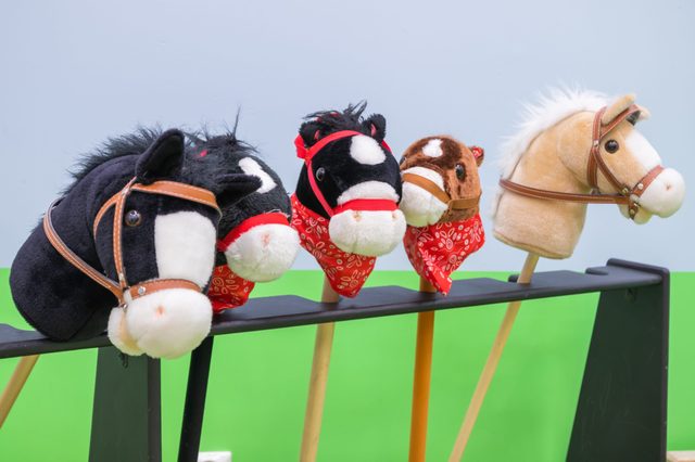 Toy hobby horses rest on a black stand, featuring colorful bandanas and a light green background.