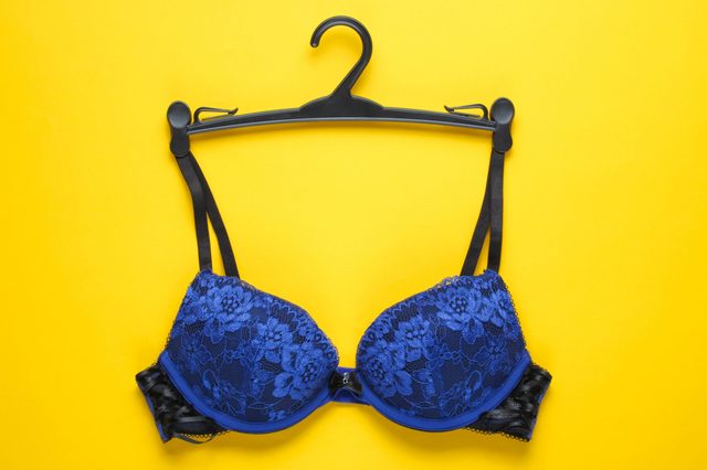 A blue lace bra on a black hanger, set against a bright yellow background.