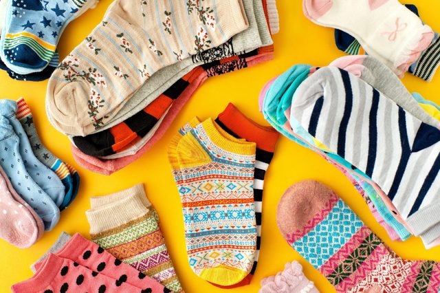 Colorful socks arranged randomly on a bright yellow background, showcasing various patterns and textures like stripes, polka dots, and floral designs.