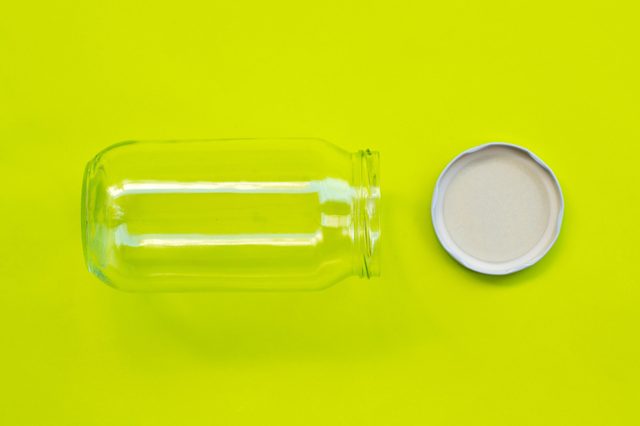 A clear glass jar lies sideways with its lid removed, set against a bright, lime green background.