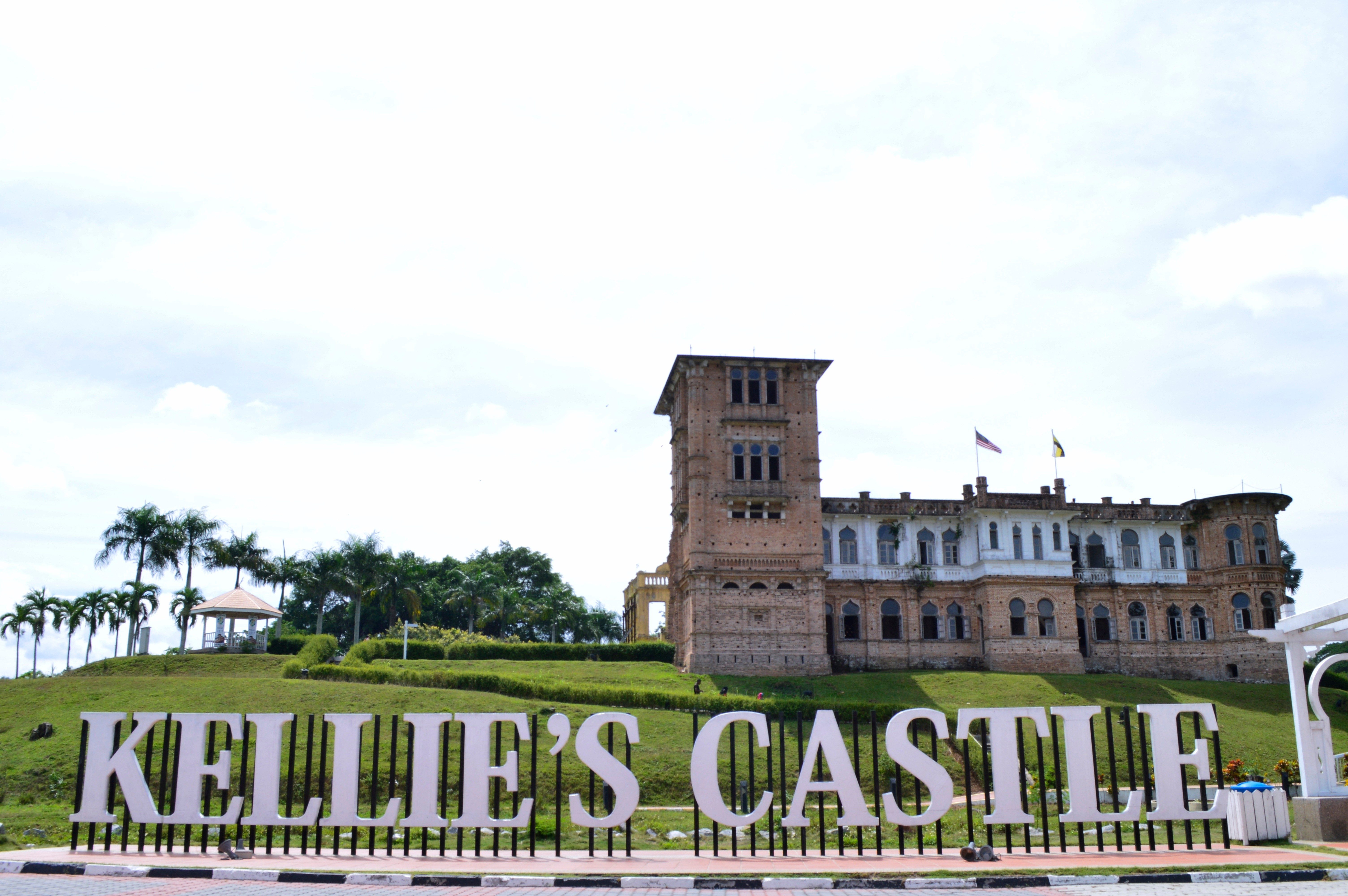 Kellie's Castle stands on a grassy hill, surrounded by palm trees, with flags flying above. Large text reads "KELLIE'S CASTLE" in the foreground.
