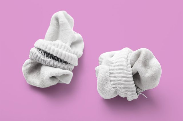 Two crumpled white socks rest on a solid pink background, displaying visible ribbed and striped patterns.