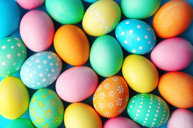 Colorful eggs lie scattered, featuring various pastel hues and patterns, against a solid blue background.