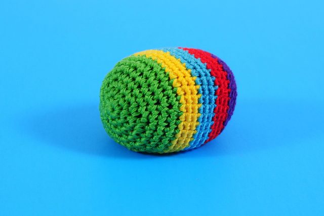 Crocheted egg-shaped object rests, showcasing rainbow-colored stripes against a bright blue background.