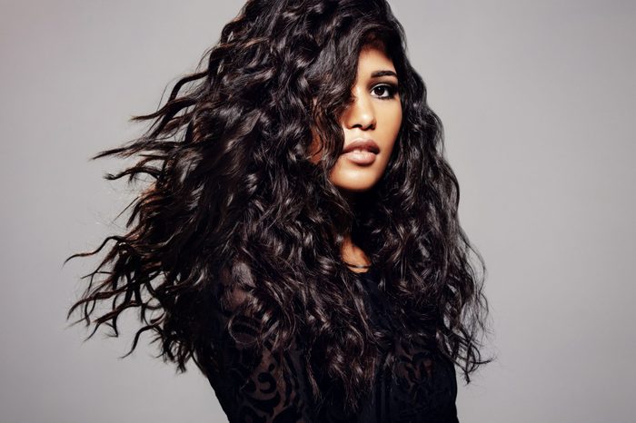 Beautiful brunette woman with long curly hair. Female fashion model with wavy hairstyle against grey background.