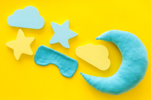 Toy shapes including a blue moon, stars, clouds, and eye mask lie on a bright yellow background.