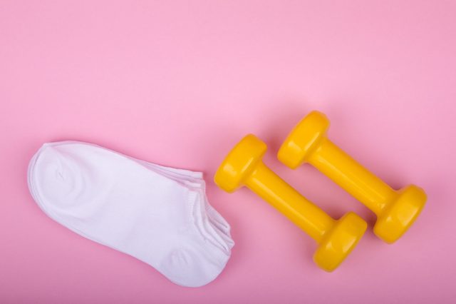 Two yellow dumbbells rest beside white socks on a pink surface.