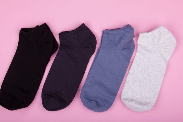 Four differently colored socks, lying side-by-side, on a pink background.