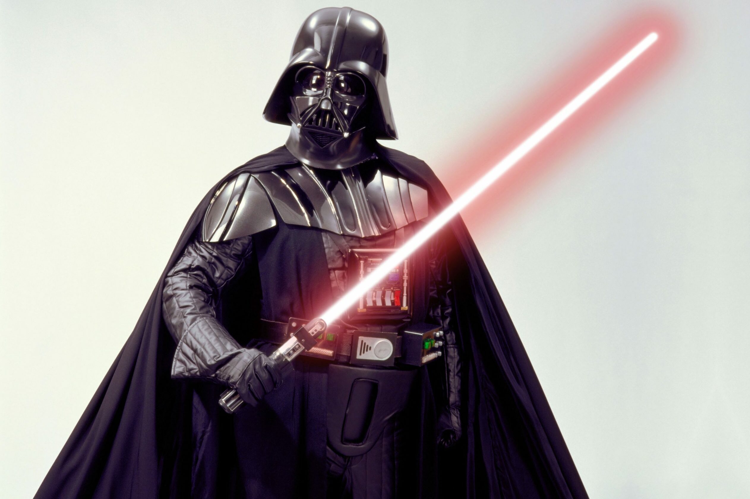 A figure in black armor wields a glowing red lightsaber against a plain background.