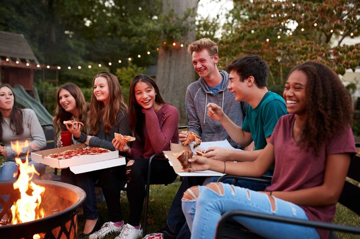 Teenagers at a fire pit eating take-away pizzas, close up