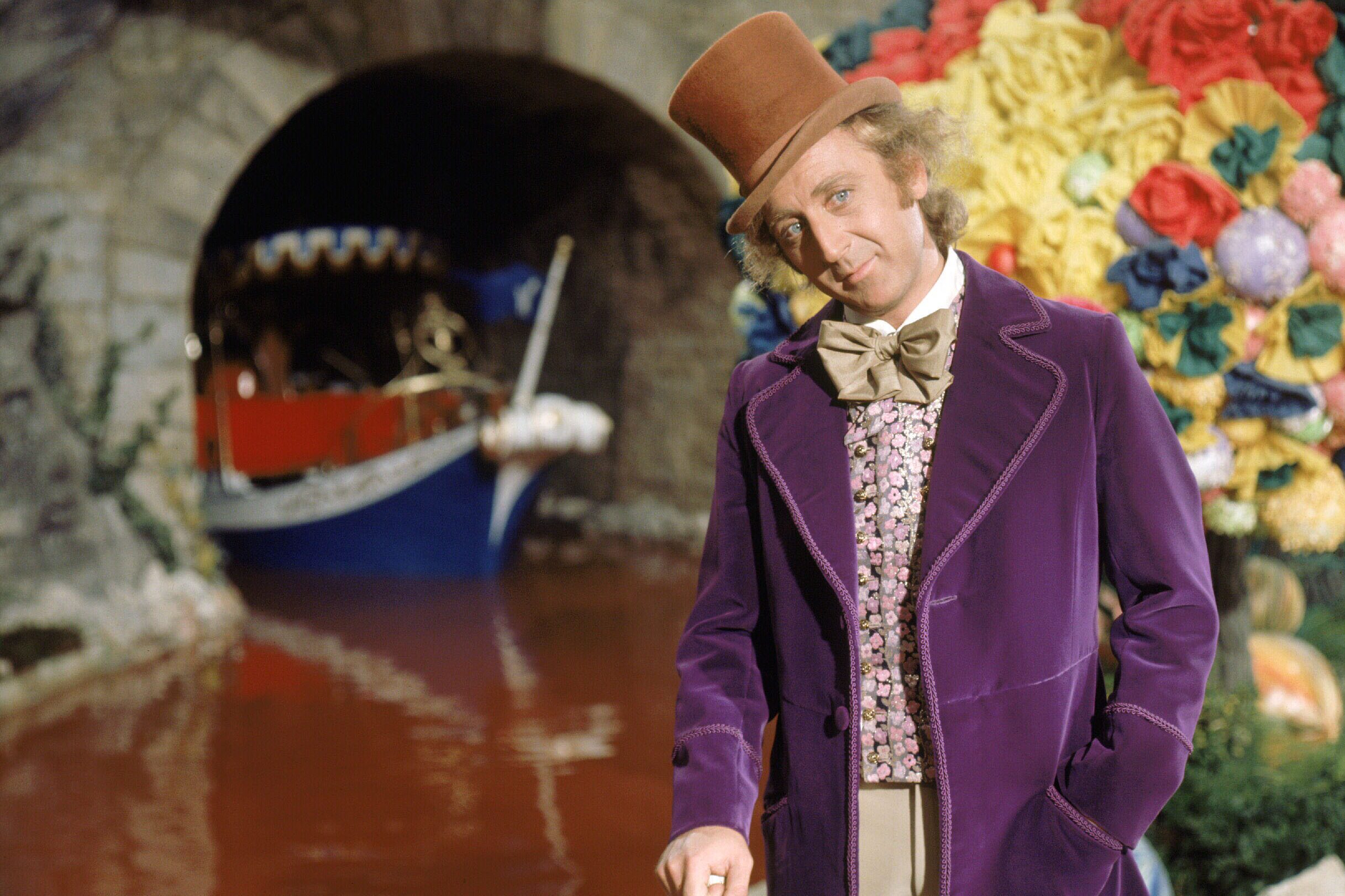 Man in a purple coat and top hat stands near a river and colorful background, with a boat approaching a tunnel.