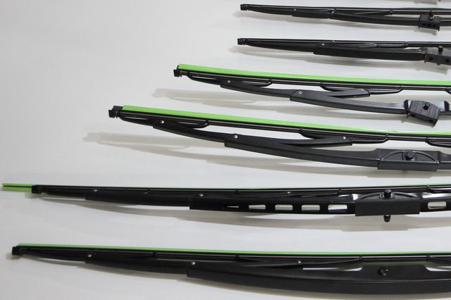 Wiper blades in various designs and sizes are aligned horizontally on a white surface.