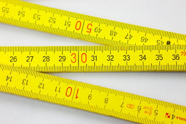 Yellow measuring tape with black and red numbers, lying on a white surface, displaying measurements from 1 to 50.