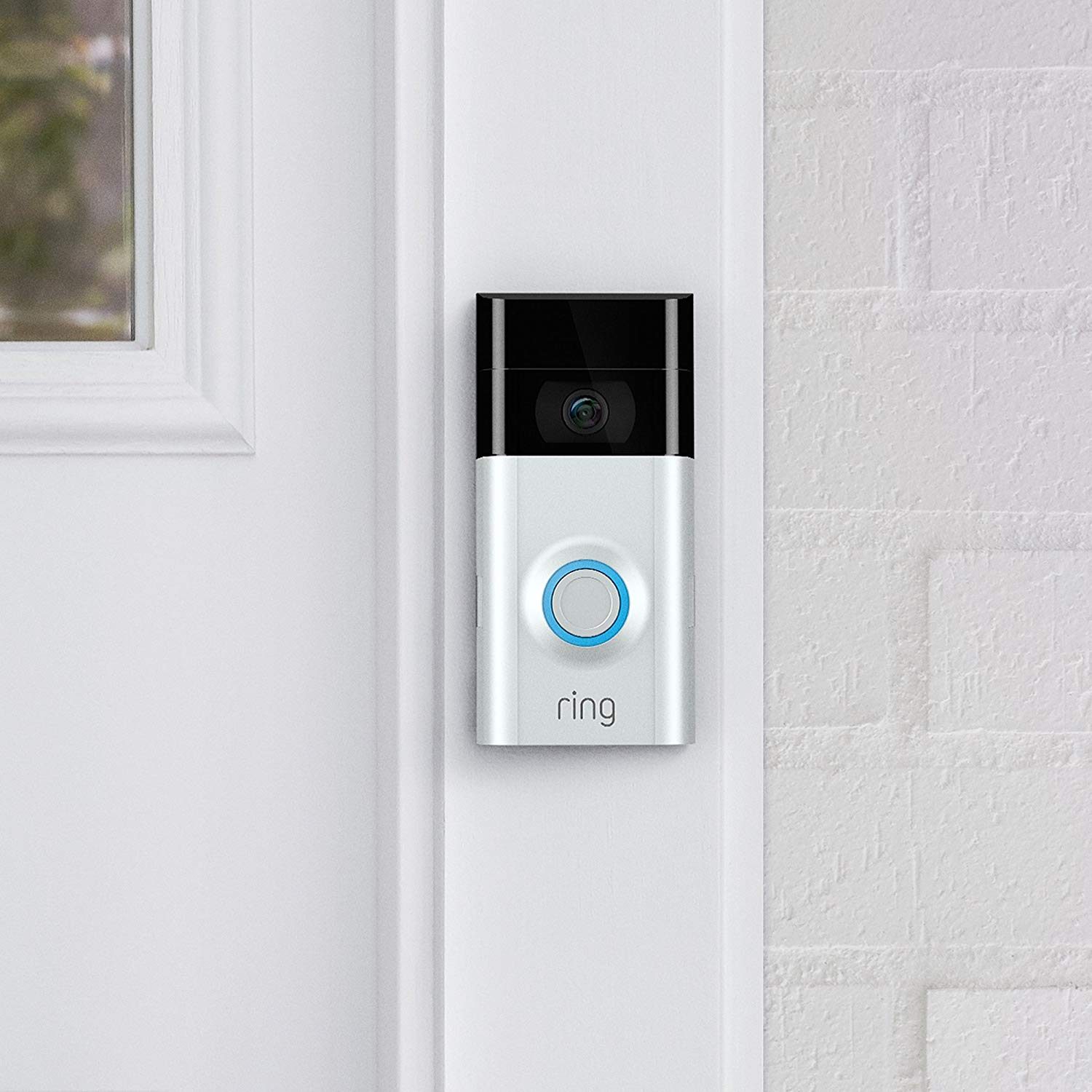 Doorbell camera with blue-lit button mounted on a white wall near a door. Text reads "ring."