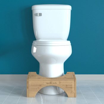 Toilet stands on tiled floor; wooden footrest labeled "Squatty Potty" positioned below, set against a teal wall backdrop.