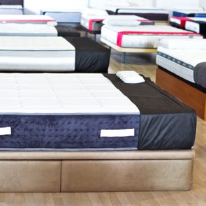 Mattresses sit on showroom floor, neatly arranged, highlighting various styles and colors on wooden flooring.