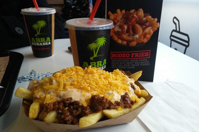 Fries covered with cheese and sauce are on a tray beside a drink cup and menu in a casual dining setting.