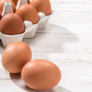 Eggs resting on a light wooden surface, with a carton of eggs partially visible in the background.