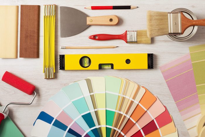Decorator holding a painting roller and painting a wooden surface, work tools and swatches at bottom, banner with copy space