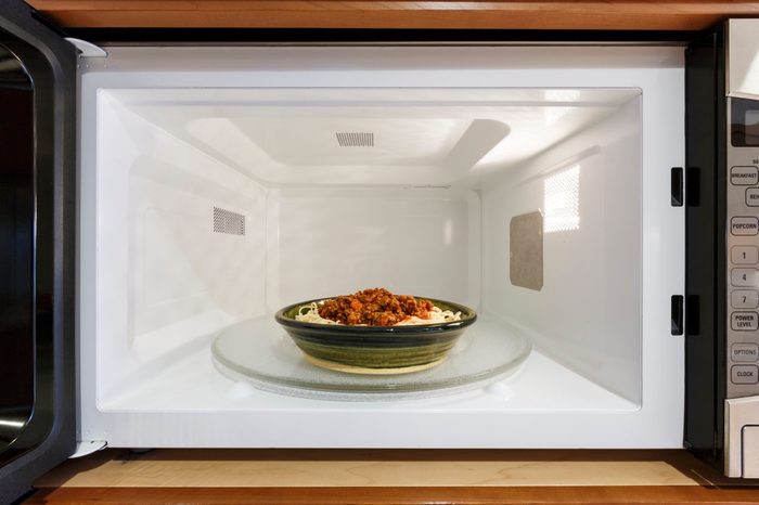 Kitchen home appliances cooking reheating plate bowl dish meal dinner of cooked spaghetti pasta with Bolognese tomato meat sauce in microwave oven