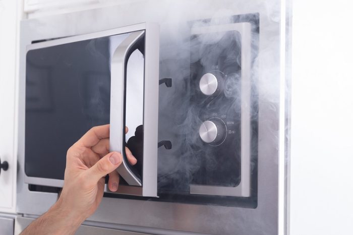 Astonished Man Standing In Front Of Burning Oven With Smoke Around Kitchen