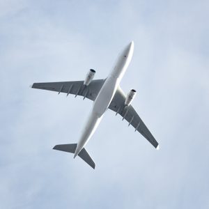 Airplane soars overhead against a clear blue sky, captured from below, highlighting its wings and engines.