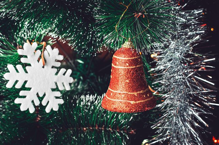 Christmas Tree Decorations: Red Orange Bell, White Snowflake, Shining Silver Tinsel on Green Needles with White Tips. Happy New Year and Christmas Concept.