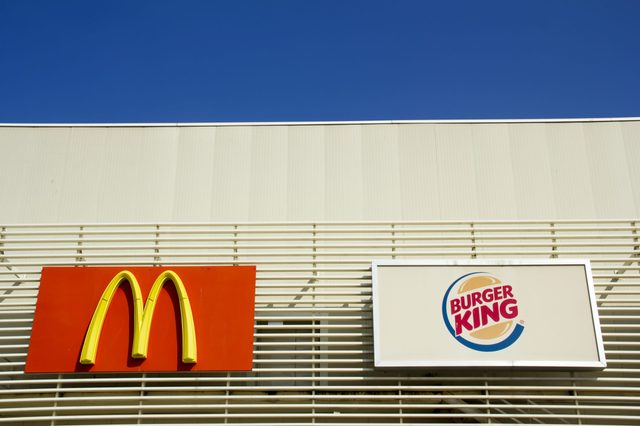 Signs display "McDonald's" and "Burger King" logos on a white building under a clear blue sky.