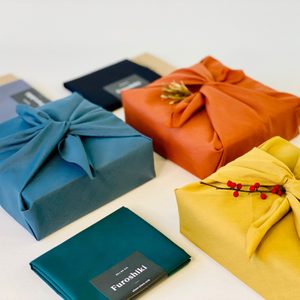 Fabric-wrapped gifts sit adorned with twine and berries on a surface; green package labeled 