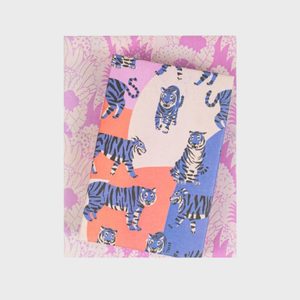Notebook covered in colorful tiger illustrations, lying on a pink patterned surface.