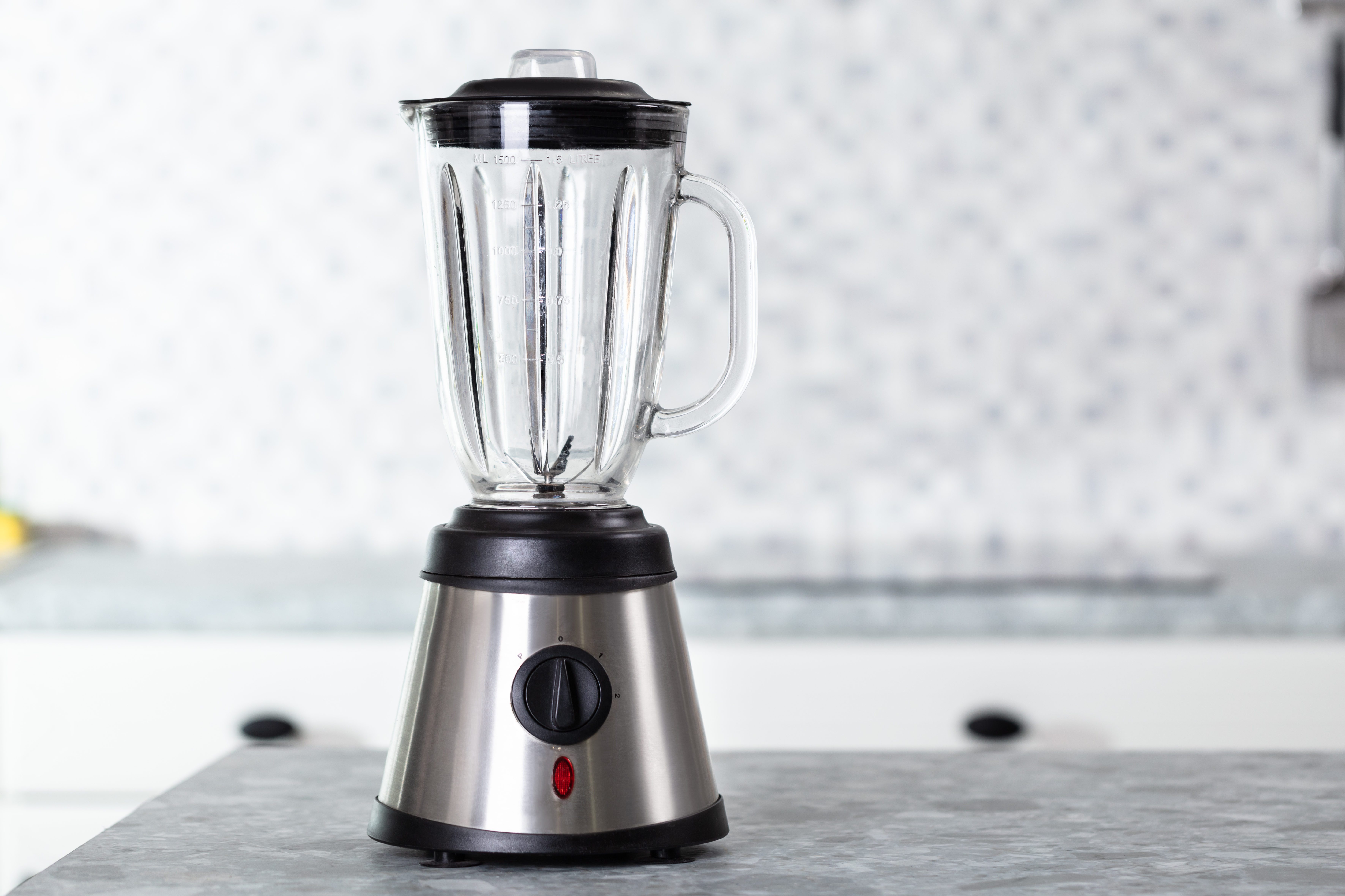 Blender sits idle on a marble countertop; a modern kitchen with a tiled backsplash provides a clean, minimalist backdrop.